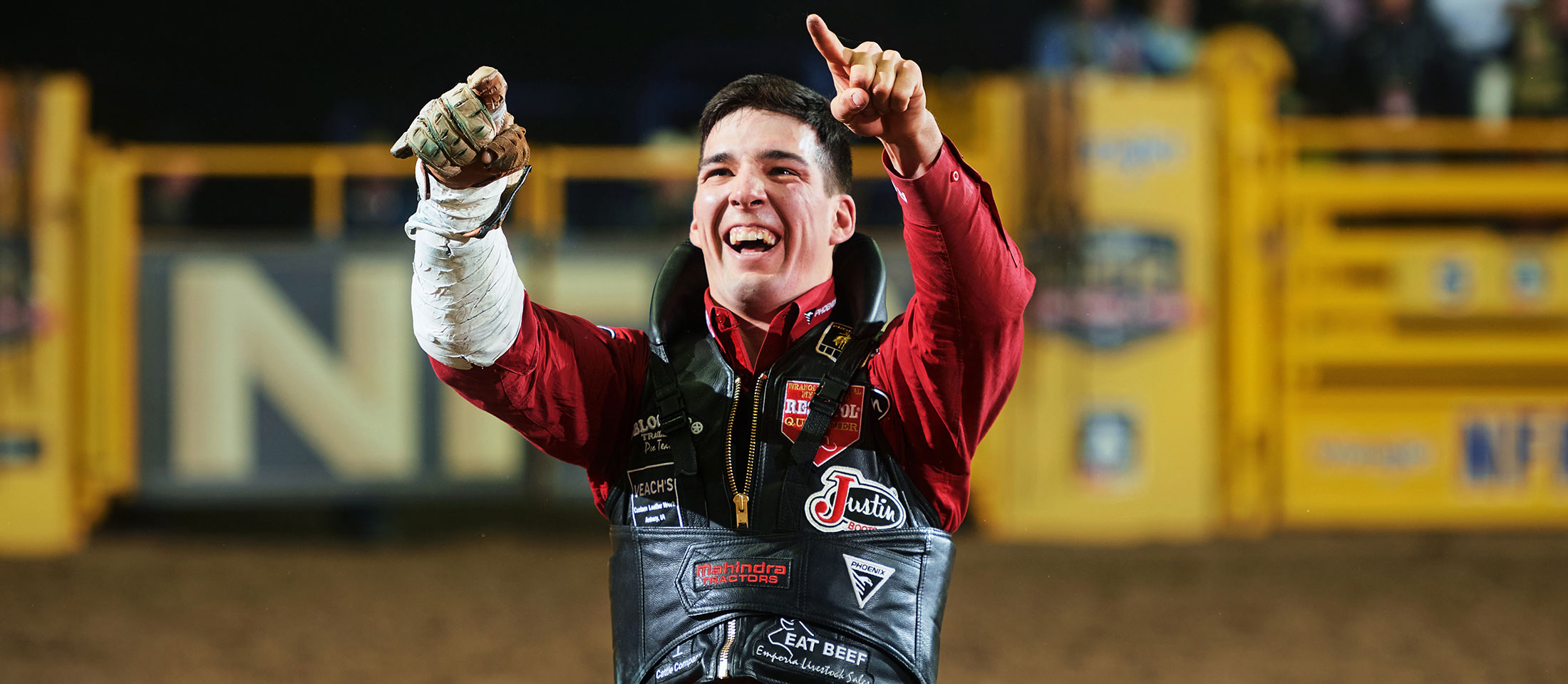 Jess Pope smiling and pointing up with both hands wearing his bareback riding equipment.